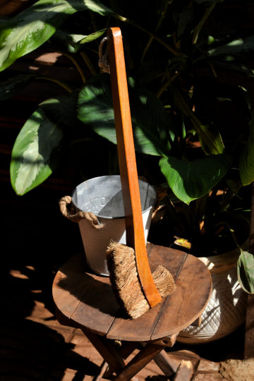 Biodegradable toilet cleaning brush with sturdy wooden grip and eco-friendly coir bristles, leaning on a stool with tropical leaves in the background.