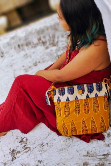 Young woman in a red dress with an Almitra Sustainables hand block printed sling bag in mustard yellow and cream, styled with bold Indian-inspired patterns and an artisan-crafted braided strap.