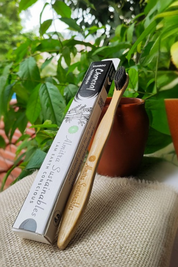 Almitra Sustainables bamboo toothbrush with charcoal bristles and eco-packaging placed in natural setting with greenery