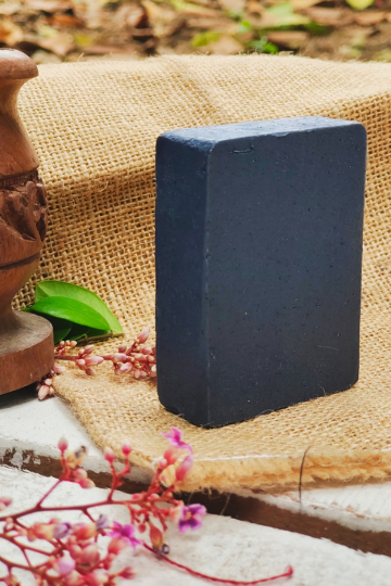 Dark brown handmade chocolate coffee soap placed on jute fabric with flowers and a rustic wooden base.