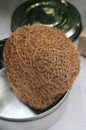 Close-up view of a natural coconut coir scrubber resting on a steel container, highlighting its fibrous texture and eco-friendly material – perfect for zero-waste kitchen cleaning.