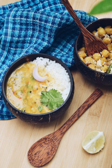 Coconut bowls filled with dal, rice, and chickpeas, served with wooden spoons—perfect for sustainable and natural meal plating.
