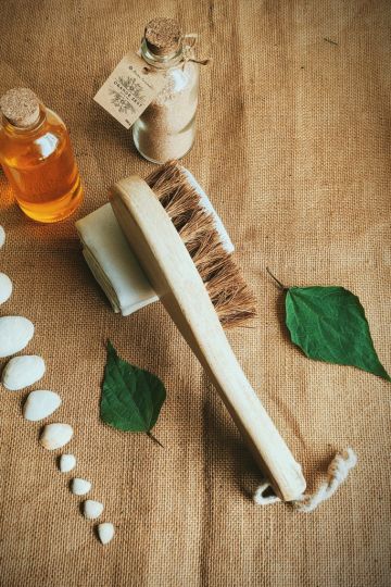 Eco-friendly dry body brush made from coconut fiber bristles and a sustainable wooden handle, displayed on a cloth with natural wellness products – ideal for zero-waste skincare routines.