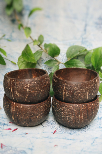 Stacked natural coconut shell bowls on a blue fabric with green leaves, ideal for eco-friendly dining and sustainable kitchens.
