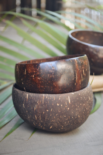Two stacked natural coconut bowls with polished finish on a palm leaf backdrop – sustainable and reusable kitchenware.