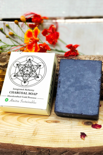 Charcoal soap beside eco-packaging on wooden plank with vibrant orange flowers by Almitra Sustainables