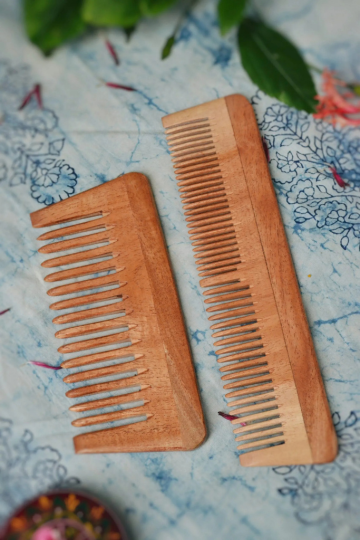 Combo pack of two neem wood combs – a small wide-tooth and a large dual-tooth comb – designed for natural hair care. Placed on a floral-printed cotton background with fresh leaves, promoting Almitra Sustainables' zero-waste beauty essentials.