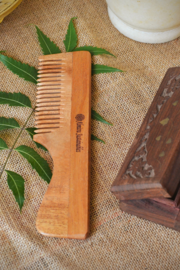 Neem wood comb with ergonomic handle from Almitra Sustainables placed on a jute background with fresh neem leaves and wooden decor, highlighting its natural, handcrafted finish and sustainability.