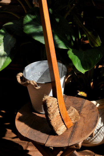 Sustainable double hockey-style toilet brush with coconut coir bristles and ergonomic wooden handle beside a rustic bucket.