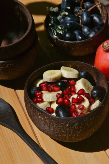 Coconut bowl with sliced bananas, grapes, and pomegranate seeds, ideal for eco-conscious fruit bowls and smoothie lovers.