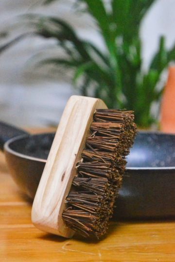 Side view of Almitra Sustainables’ natural scrub brush made from coconut coir and sustainable wood, placed upright beside cookware on a wooden kitchen surface.