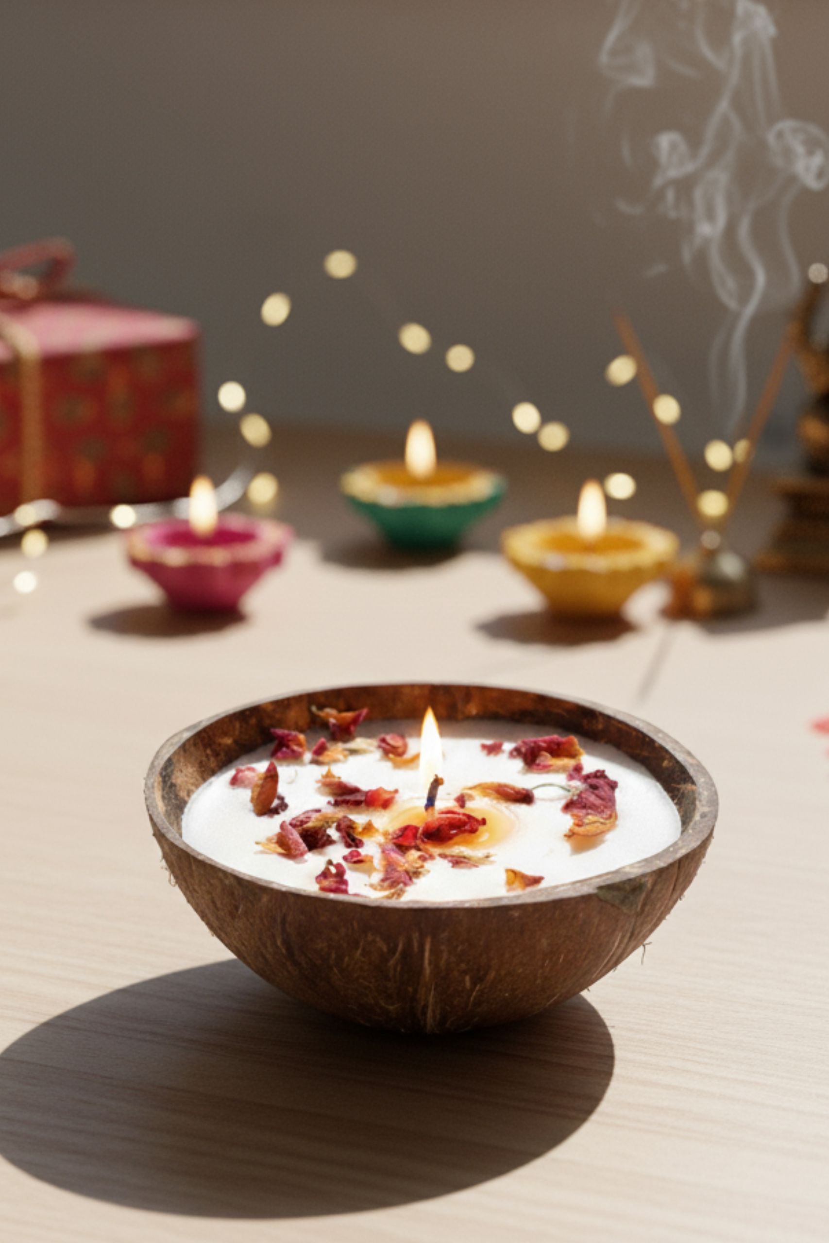 Eco-friendly soy wax candle by Almitra Sustainables in a natural coconut shell, topped with dried rose petals and lit during Diwali. Surrounded by traditional diya's, incense, and festive decor, this handmade candle is perfect for sustainable celebrations and zero-waste gifting.