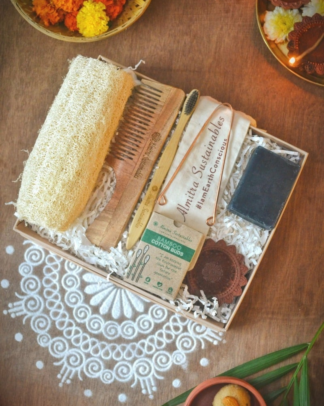 Eco-friendly self-care gift hamper by Almitra Sustainables featuring bamboo toothbrush, natural soap, wooden comb, loofah, bamboo cotton buds, and reusable pouch in sustainable packaging with festive rangoli, marigold flowers, and clay diyas — ideal zero-waste Diwali gift.