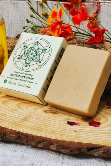 Handcrafted rosemary cold process soap bar with Almitra Sustainable eco-friendly packaging placed on a natural wooden slab with flowers and botanical oil, herbal rosemary soap made using traditional cold process method for gentle cleansing and sustainable skincare. 