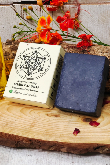 Handmade charcoal cold process soap bar by Almitra Sustainable displayed with natural packaging and flowers on wooden board.