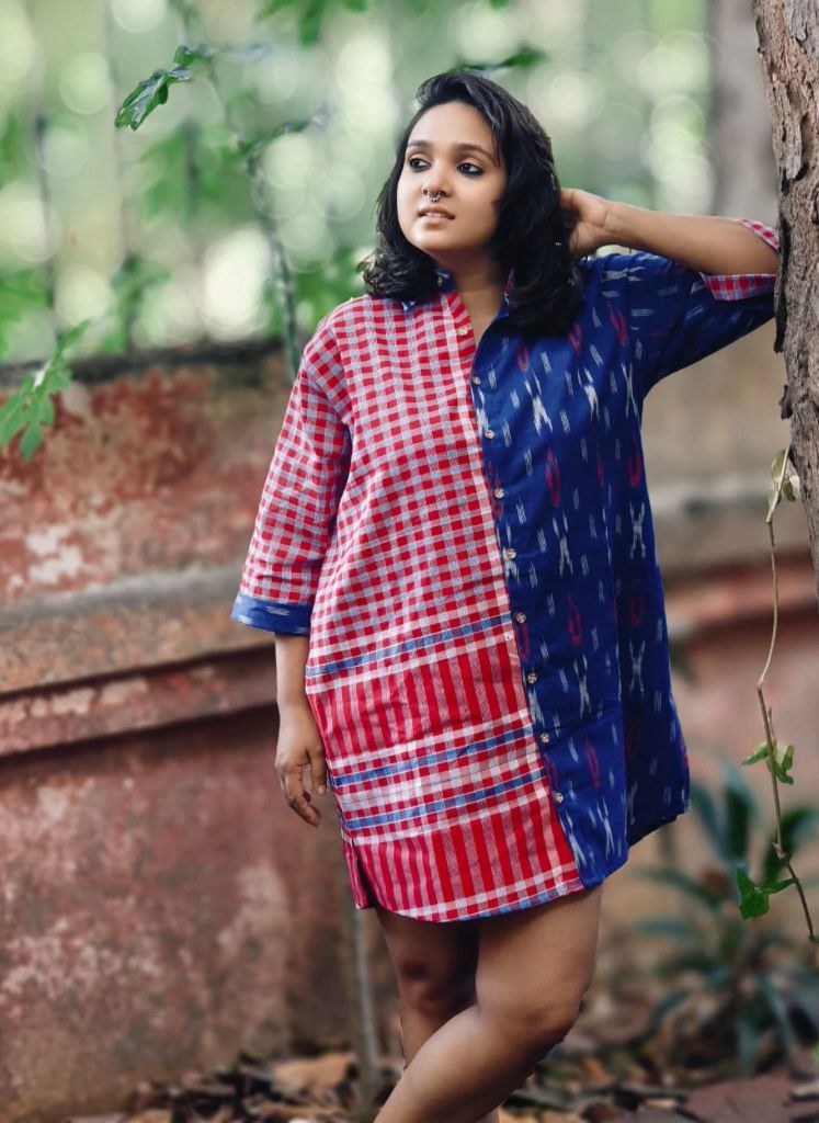 Woman wearing a red and blue checkered dress with a patterned overlay, standing outdoors.