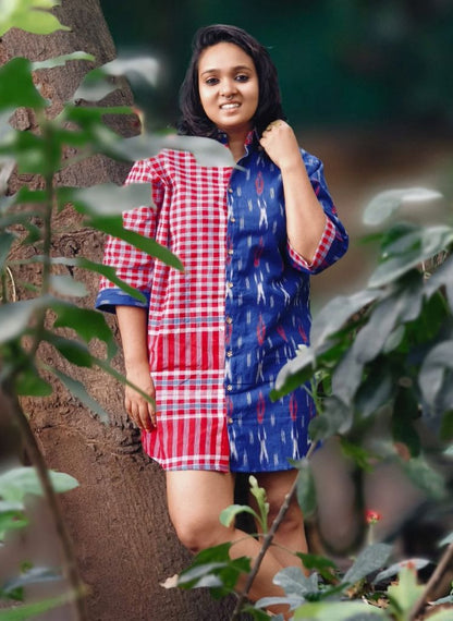 Woman wearing a red and blue checkered dress standing among green plants.