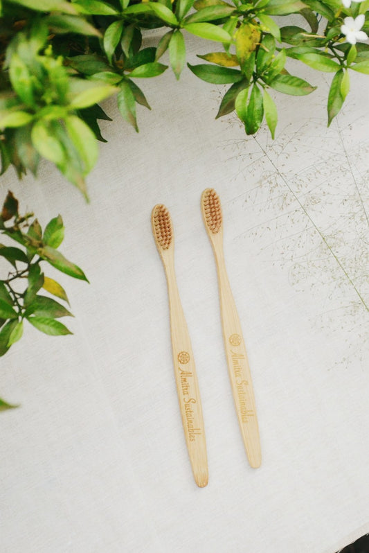 Two sustainable bamboo toothbrushes for kids with soft bristles and “Almitra Sustainables” engraved handles, placed on a fabric surface with greenery.