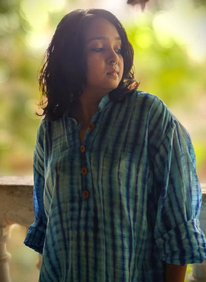 Woman wearing a blue and green patterned shirt with a blurred natural background