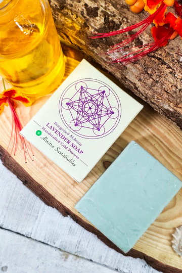 Lavender cold processed soap bar with Almitra Sustainable packaging displayed on rustic wooden slab with flowers and natural oil bottle, calming handmade soap crafted for aromatherapy, gentle cleansing and eco-conscious skincare.