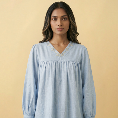 Woman wearing a light blue top with intricate fish details on a beige background