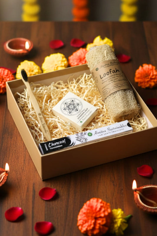 Eco-friendly festive gift hamper by Almitra Sustainables featuring a bamboo toothbrush, natural soap bar, charcoal toothpowder, and biodegradable loofah in sustainable packaging, surrounded by marigold flowers, diya's, and rose petals — perfect zero-waste Diwali gift.